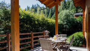A wooden deck with a table and chairs, surrounded by a wooden fence and lush greenery. - Miranda by Interhome (Champex)