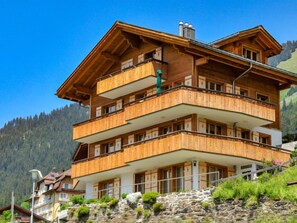 Ein mehrstöckiges Holzchalet mit Balkonen vor einer Bergkulisse.
