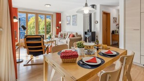 Uma sala de jantar com uma mesa de madeira posta para quatro pessoas, um sofá e uma lareira ao fundo.