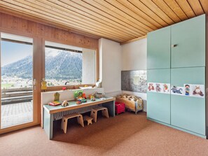A child's playroom with a wooden desk, toys, and a view of mountains through a large window.