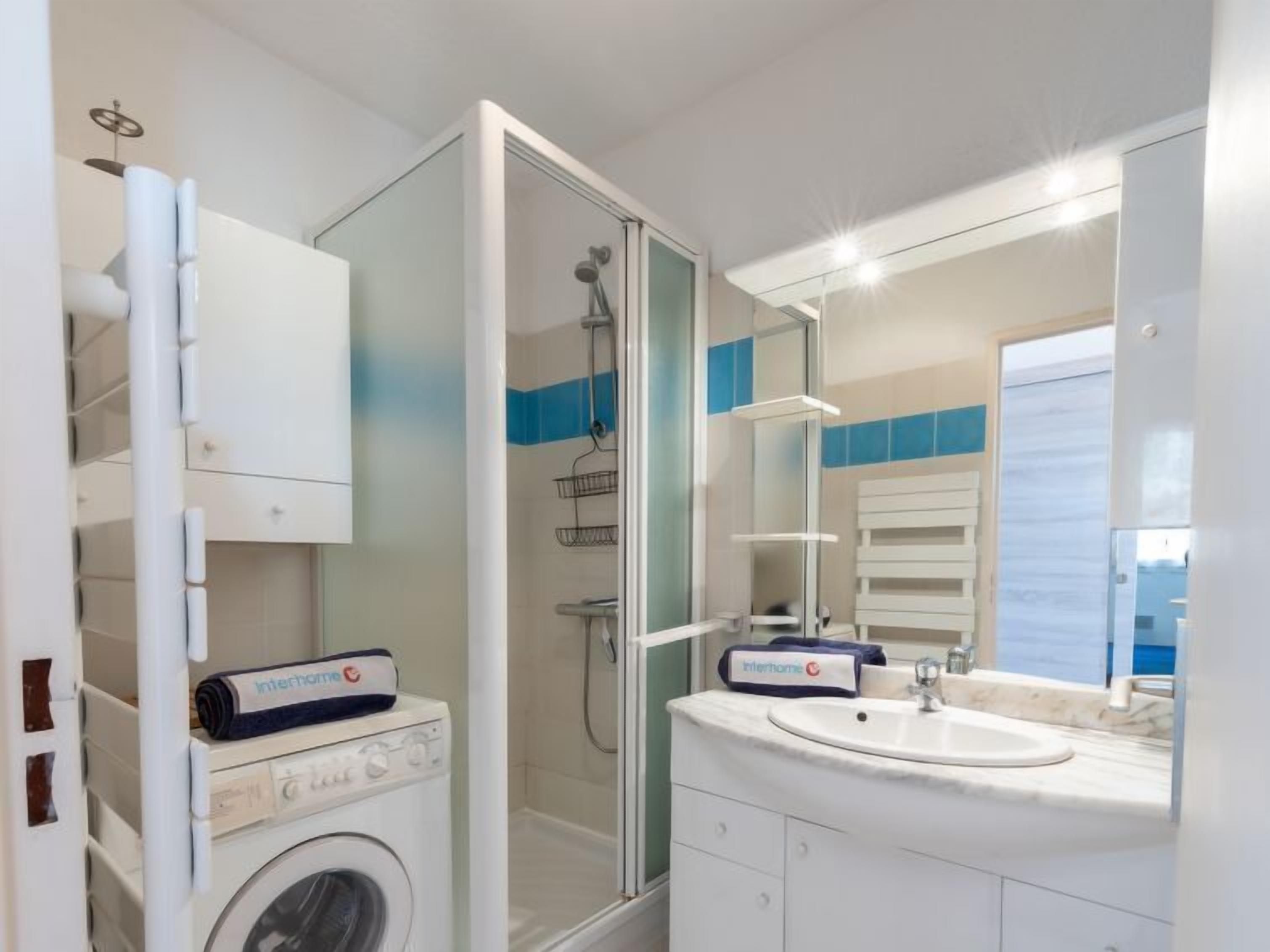 A modern bathroom with a glass-enclosed shower, a built-in washing machine, and a vanity with a sink.