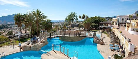 A large outdoor swimming pool with multiple levels and a surrounding deck area, set against a backdrop of palm trees and a cityscape.