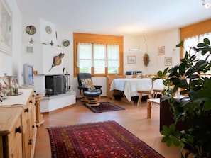 A cozy living room with a fireplace, a dining area with a table set for two, and a large window with curtains.