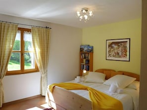 A bedroom with a bed, a window with curtains, a bookshelf, and a painting on the wall.
