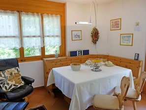 A cozy room with a wooden bench, a table with a white tablecloth, and a chair with a floral cushion.