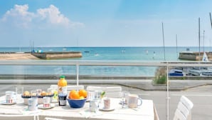 Une table dressée avec des aliments pour le petit-déjeuner, donnant sur une plage et un port de plaisance.