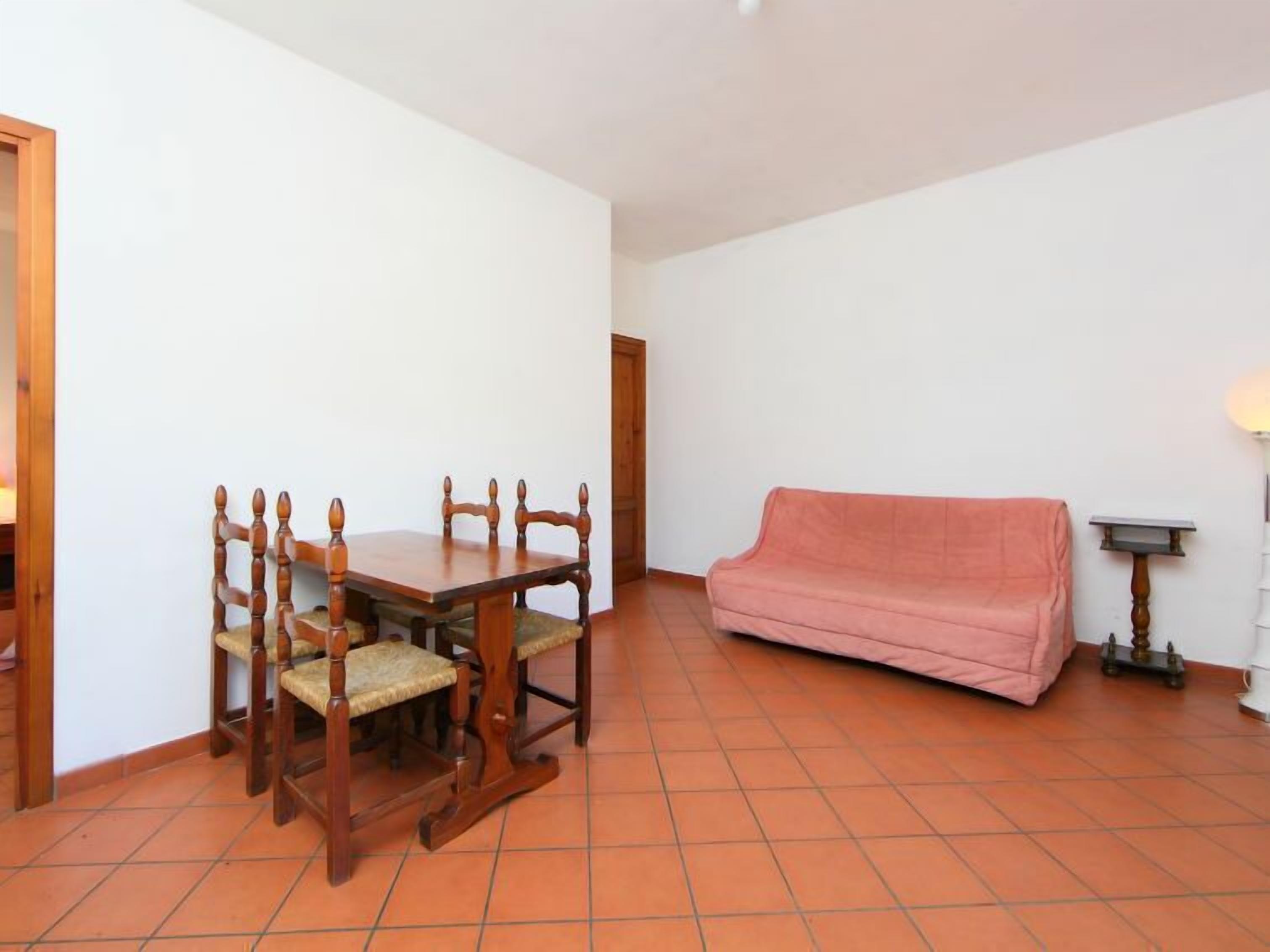A dining area with a wooden table and chairs, a pink sofa, and a lamp.