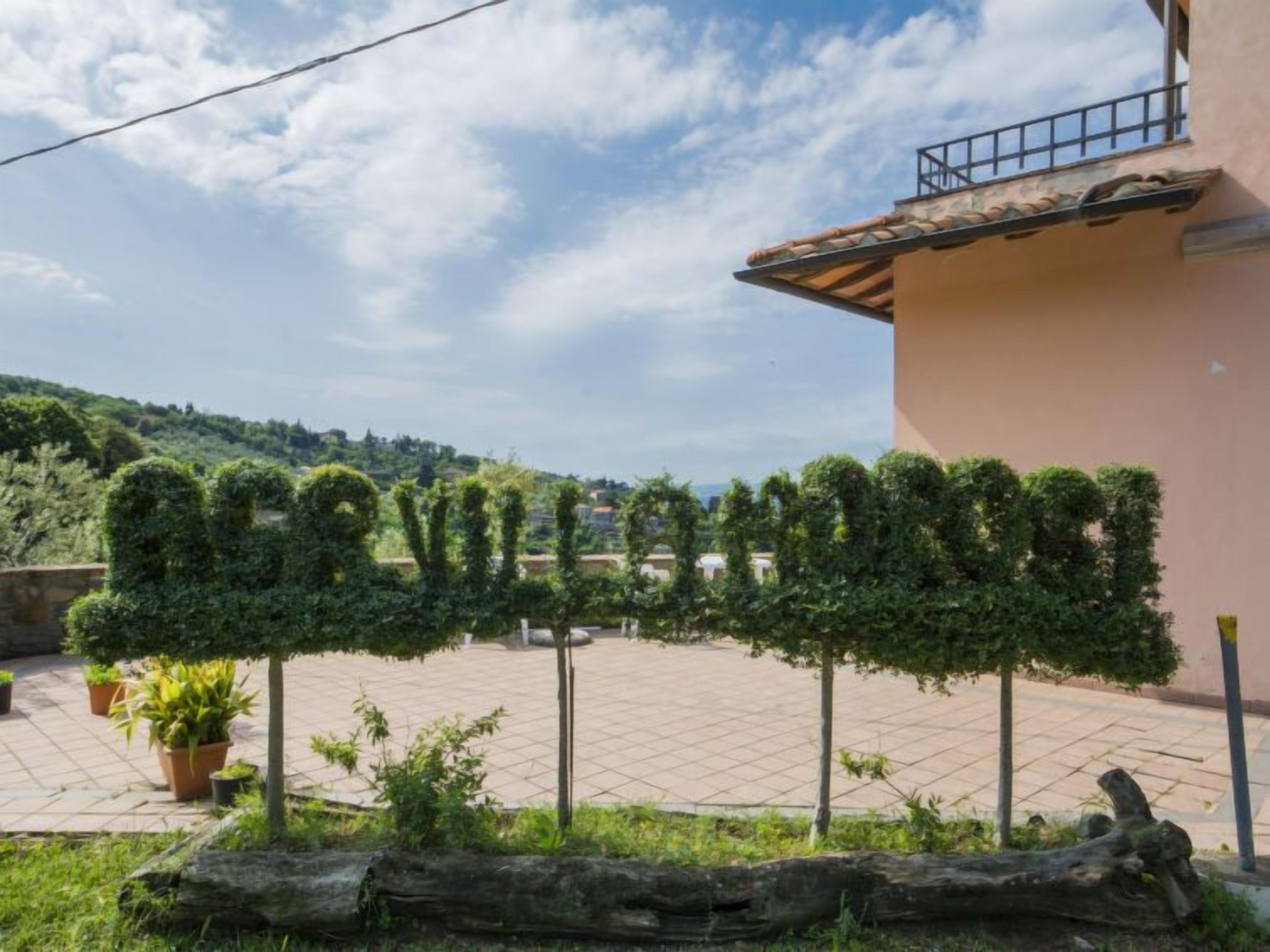 A courtyard with neatly trimmed hedges spelling out "CULTURE," a tiled floor, and a building with a balcony.