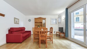 A living room with a red sofa, wooden dining table, chairs, a TV, and a cabinet. - Platja de Roses by Interhome (Roses)