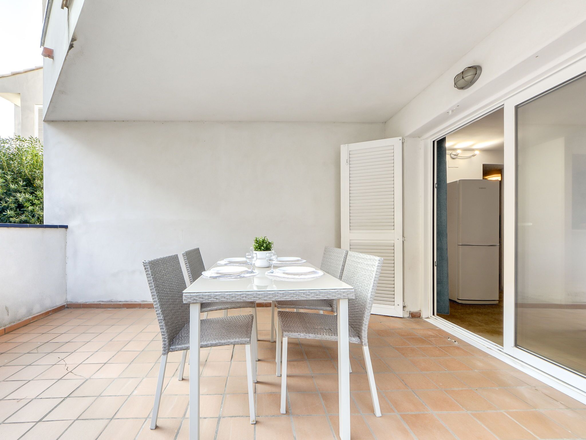 A dining area with a table set for four, surrounded by wicker chairs, on a tiled floor.