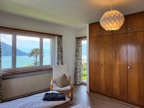 Een slaapkamer met een bed, een stoel, een kledingkast en uitzicht op zee.