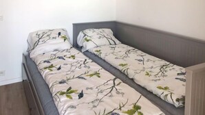 Ein kleines, ordentlich eingerichtetes Schlafzimmer mit zwei Einzelbetten, jeweils mit blumigem Bettbezug.
