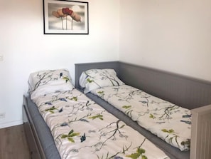 Une petite chambre à coucher, bien rangée, avec deux lits simples, chacun agrémenté de draps à motifs floraux.