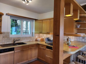 A kitchen with wooden cabinets, a window, and a countertop with a coffee machine. - Stellina del Sole by Interhome (Brissago)