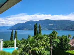 A view of a lake with mountains in the background, a pool area with palm trees, and a clear sky.