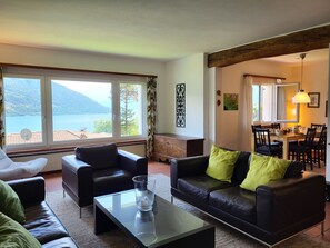 Un salón con vistas a un lago y montañas, amoblado con sofás de cuero y una mesa de centro de vidrio.