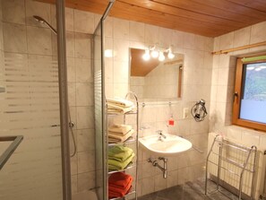 Un bagno con doccia, lavandino, specchio e porta asciugamani.