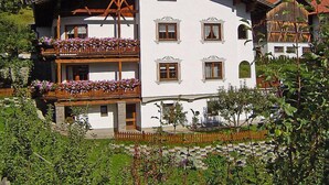 Ein zweistöckiges Gebäude mit Balkonen, die mit Blumen geschmückt sind, umgeben von Grün und Bergen.