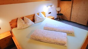 Ein Schlafzimmer mit Holzboden, einem Bett mit floralem Bettzeug, einem Nachttisch, einem Sessel und einer Wandleuchte.