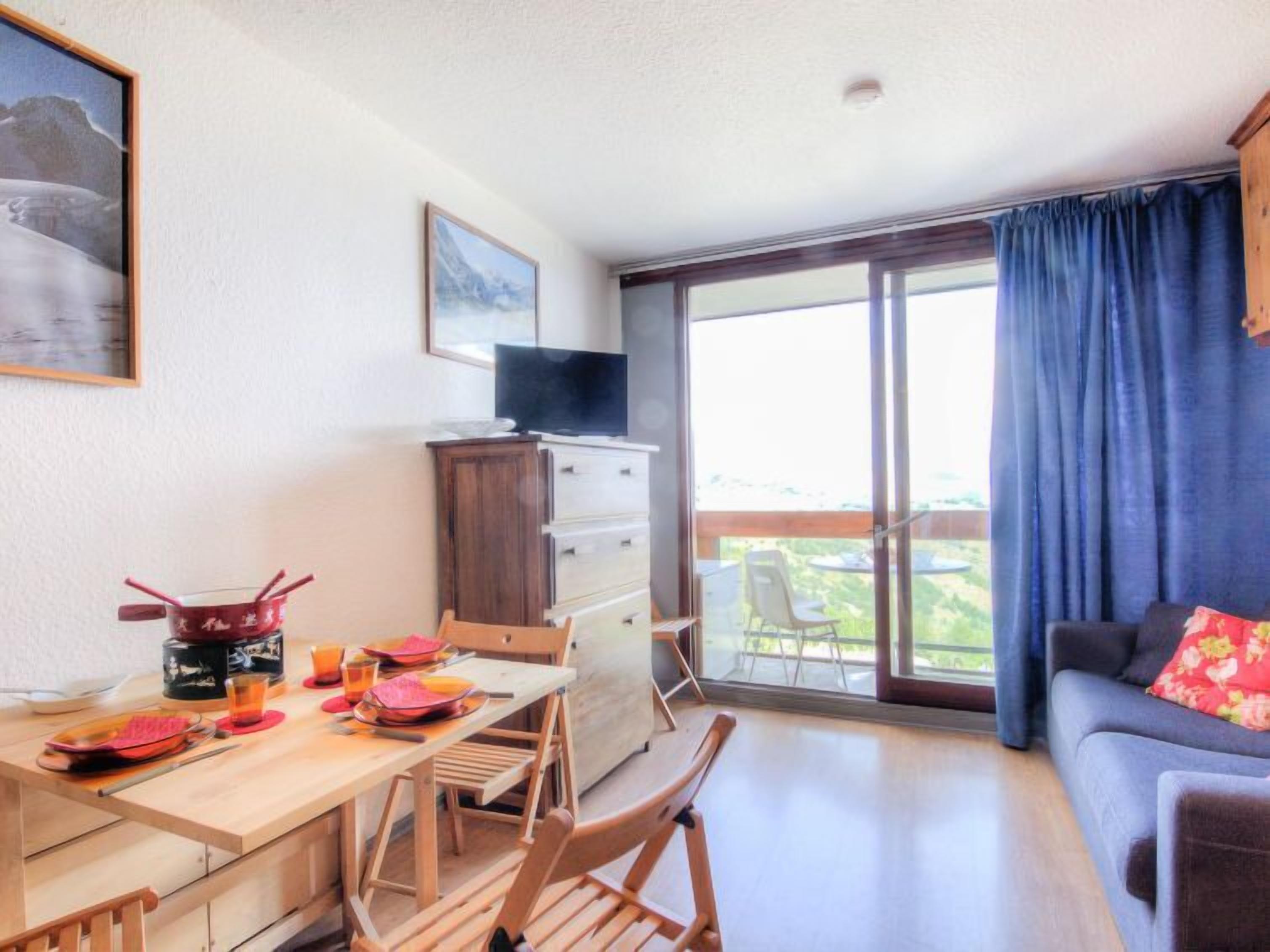 Una stanza con un tavolo da pranzo apparecchiato per due, un divano, una TV su un mobile e un balcone con vista.