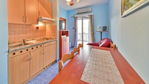 A compact kitchen with wooden cabinets, a built-in stove, and a dining area with a table and chairs. - Apartment Delfin by Interhome (Karlobag)