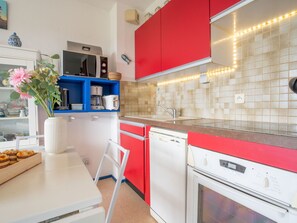 A kitchen with red cabinets, a white countertop, a white dishwasher, and a white oven. - Plein Sud by Interhome (Quiberon)