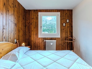 A bedroom with a wooden wall, a window with a view of trees, a radiator, and a wooden hanger. - Fienili di Brenta 13 by Interhome (Madonna di Campiglio)