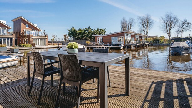 A wooden deck with a table and chairs overlooking a canal with boats. - Busch en Dam by Interhome (Uitgeest)