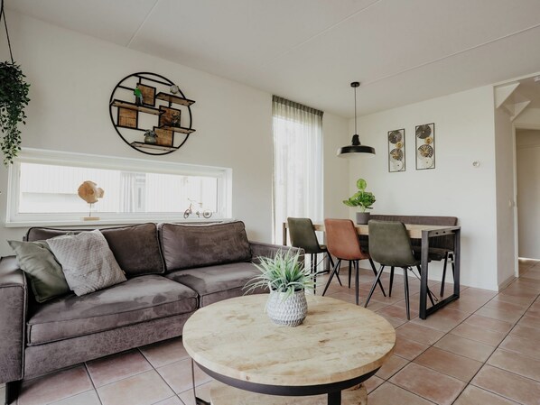 Una sala de estar con un sofá gris, una mesa redonda con una planta, y un comedor con sillas y una mesa.