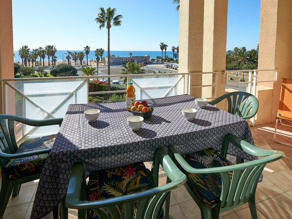 A balcony with a table set for two, overlooking a beach with palm trees and the sea. - Cap Hermes by Interhome (Fréjus)