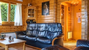 Interior acolhedor de cabana com sofá de couro, paredes de madeira, armário e janela com cortinas.