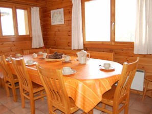 Una cabaña de madera con una mesa redonda para el desayuno, rodeada de sillas de madera.