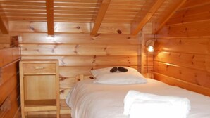 Quarto de cabana de madeira com cama, mesa de cabeceira e luminária na parede.