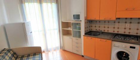 Eine kleine Küche mit orangenen Schränken, einer Waschmaschine und einer Mikrowelle.