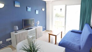 Un salon moderne avec un canapé bleu, un téléviseur à écran plat, une petite table et une plante en pot.