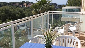 Un balcon avec une nappe bleue, des chaises blanches et un pot de fleurs.