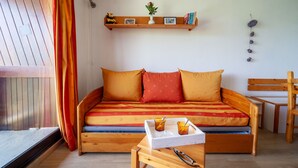 Et hyggeligt rum med en træsofa, et lille bord med glas og en hylde med bøger og en plante.