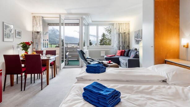 Een hotelkamer met balkon, eethoek en een bank.