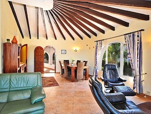 A spacious living area with a green sofa, a leather couch, a dining table with chairs, and a view through a large window.