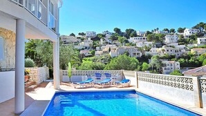 A swimming pool with lounge chairs, a view of a hillside with buildings, and a white building with a balcony. - Balcon Al Mar by Interhome (Jávea)