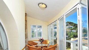 A balcony with wicker furniture, a table with a vase, and a view of a hillside with buildings. - Balcon Al Mar by Interhome (Jávea)