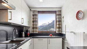 Et kompakt køkken med moderne design, der indeholder en indbygget ovn, en stålvask og et vindue med udsigt til et bjerglandskab.