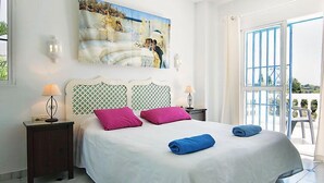 Ein Schlafzimmer mit einem großen Bett, zwei Nachttischen, einem Gemälde über dem Bett und Blick durch eine Glastür.