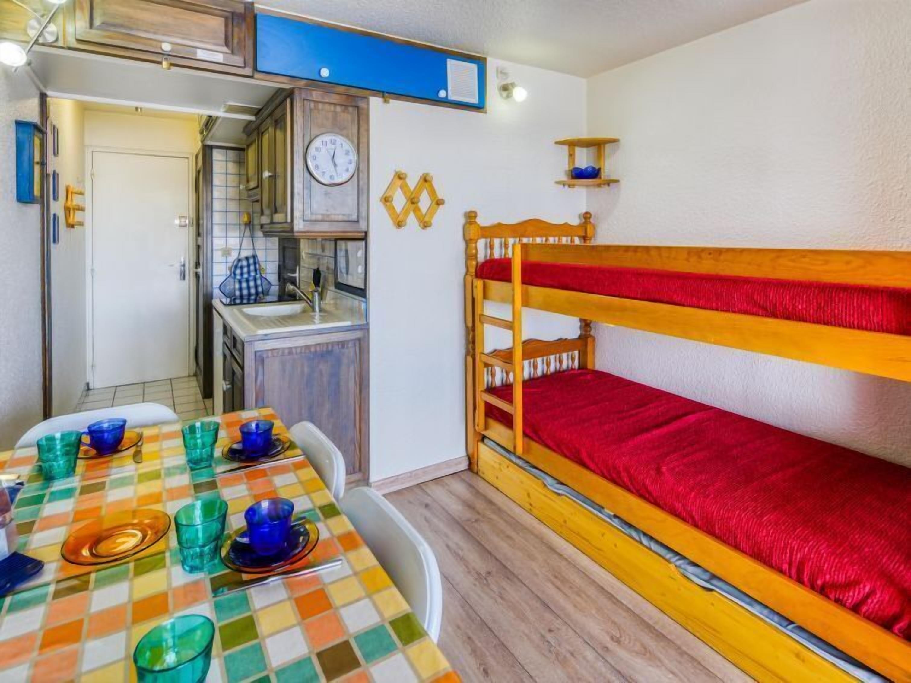 Een compacte kamer met een stapelbed, een kleine kitchenette en een eettafel met kleurrijk servies.
