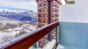 A high-rise building with a view of snow-covered mountains and a winding road below. - Soyouz Vanguard by Interhome (Le Corbier)