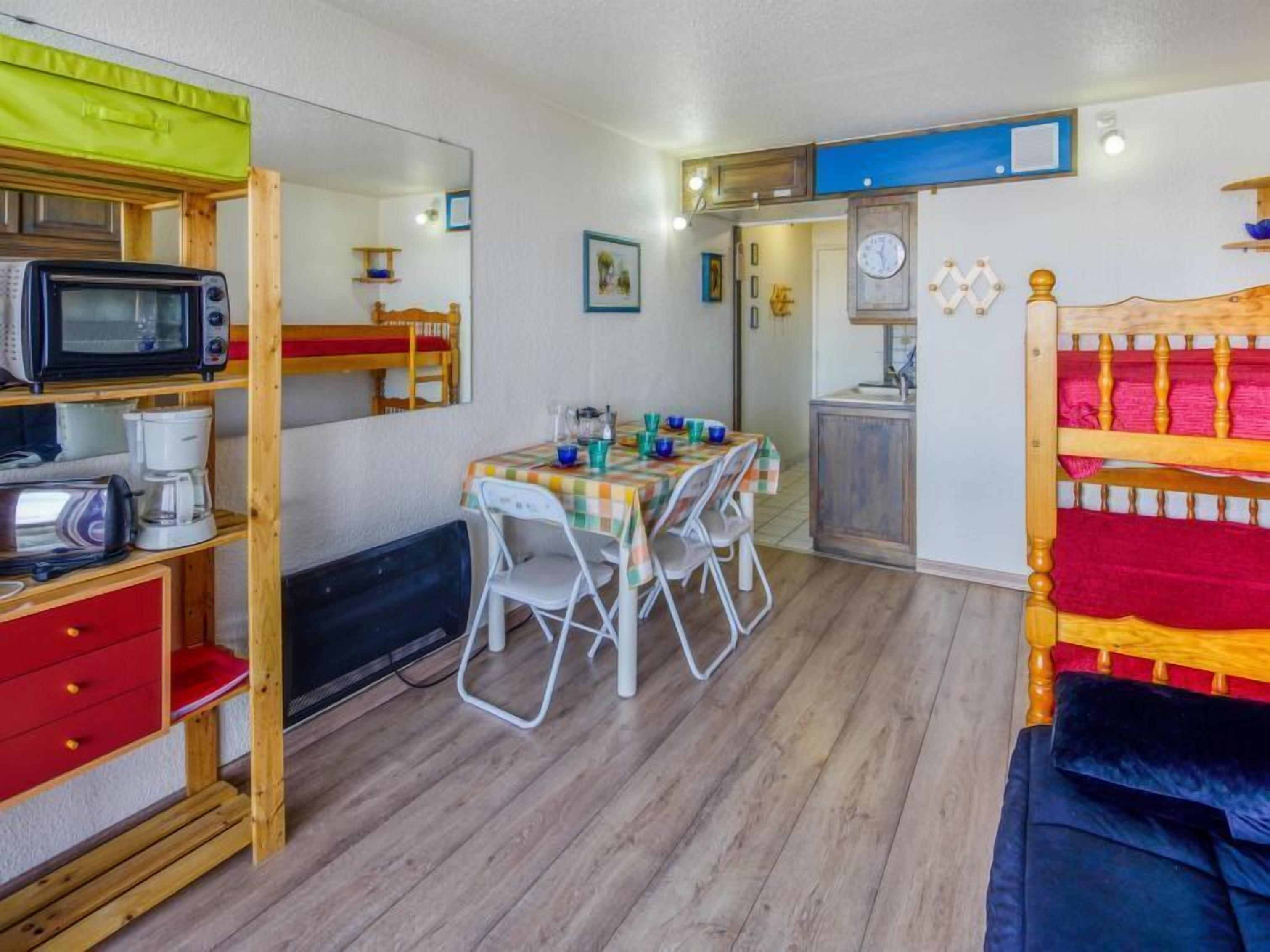 Habitación compacta con una mesa de comedor, sillas, microondas, cafetera y cama con cabecera colorida.