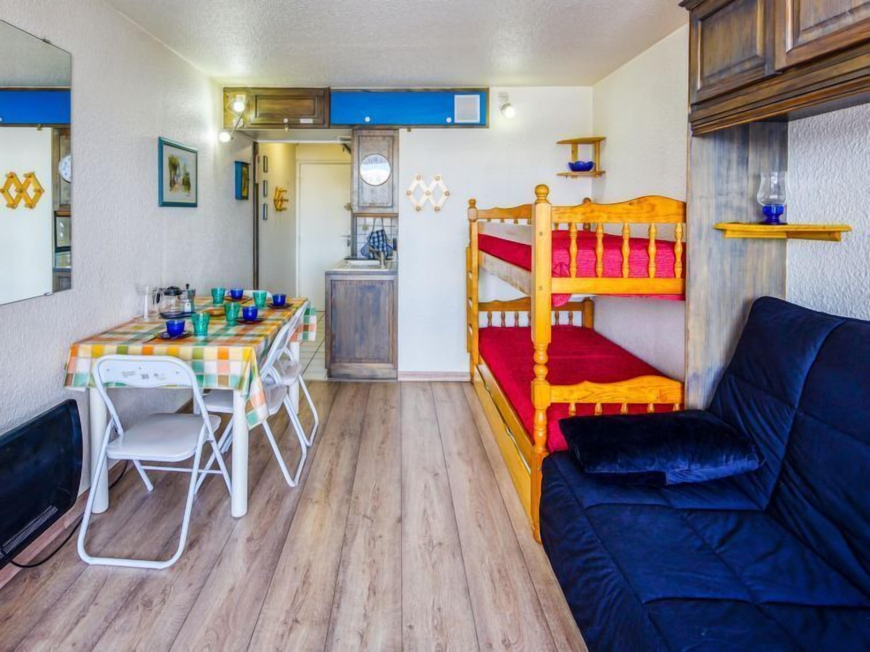 A compact room with a bunk bed, a dining table with chairs, a small kitchenette, and a sofa.