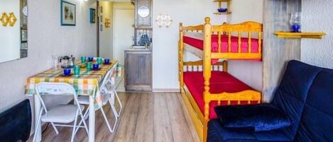 A compact room with a bunk bed, a dining table with chairs, a small kitchenette, and a sofa.