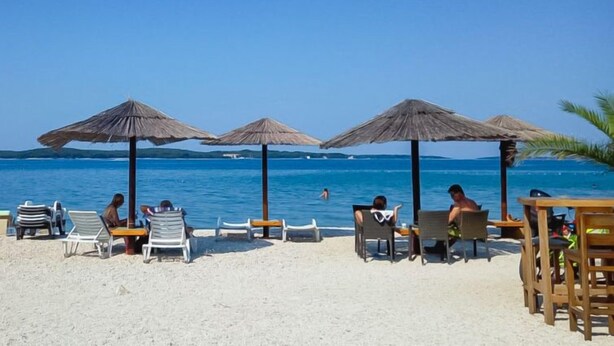 Une plage avec des chaises longues et des parasols, un ciel bleu dégagé et une mer calme.