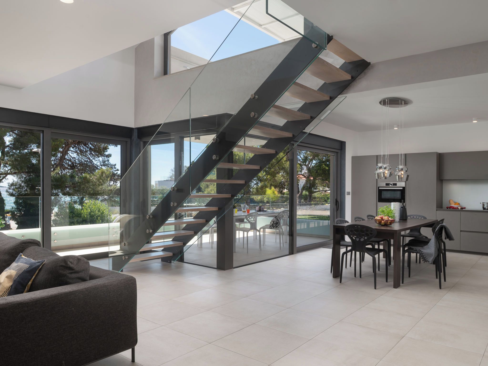 Ein modernes Interieur mit einer Glaswendeltreppe, einem Essbereich und einer Küche.